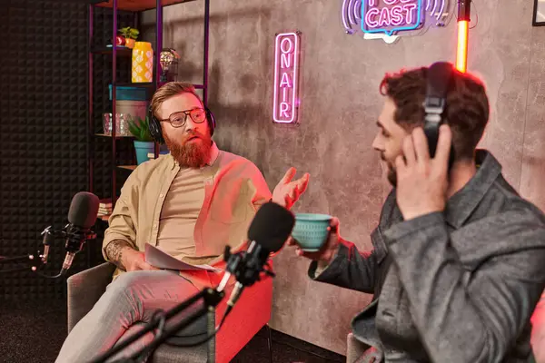 Entrevistador guapo con un atuendo elegante discutiendo preguntas con su joven invitado durante el podcast - foto de stock