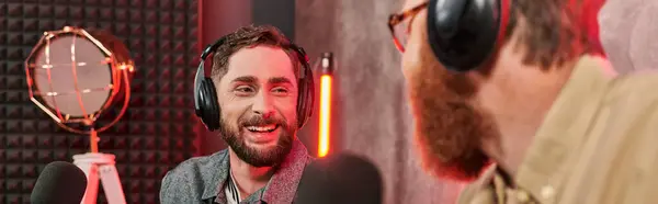 Hombres guapos barbudos en trajes elegantes con auriculares que hablan activamente durante el podcast, pancarta - foto de stock