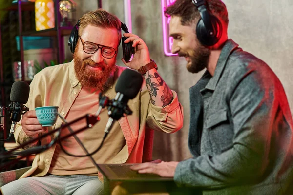 Cheerful men in comfortable attires with coffee and laptop during their discussion on podcast — Stock Photo