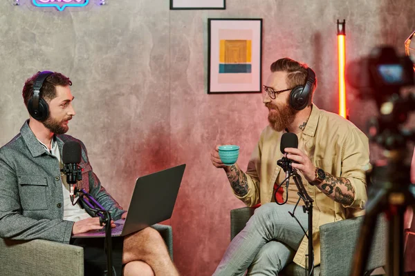 Hommes gais dans des vêtements confortables avec café et ordinateur portable lors de leur discussion sur podcast — Photo de stock