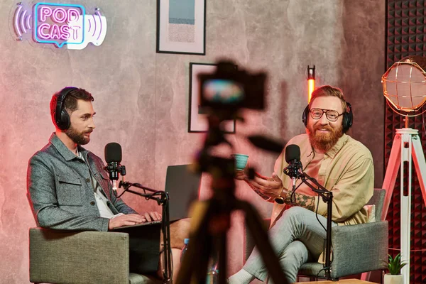 Hommes gais dans des vêtements confortables avec café et ordinateur portable lors de leur discussion sur podcast — Photo de stock