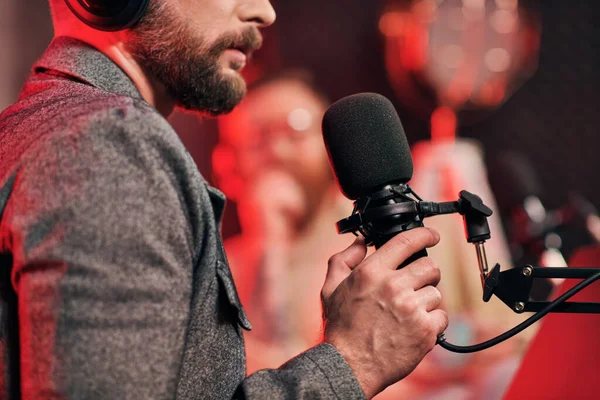 Cropped focused view of bearded man with microphone with his blurred interviewer on podcast — Stock Photo