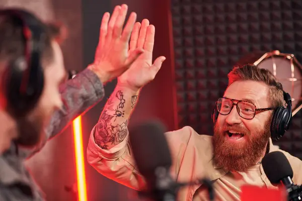 Bearded interviewer with glasses doing high five with his blurred guest during their podcast — Stock Photo