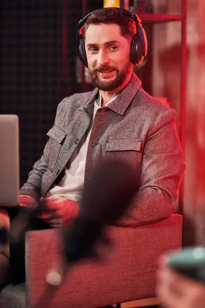 Handsome bearded man with headphones in casual outfit sitting during podcast while in studio — Stock Photo