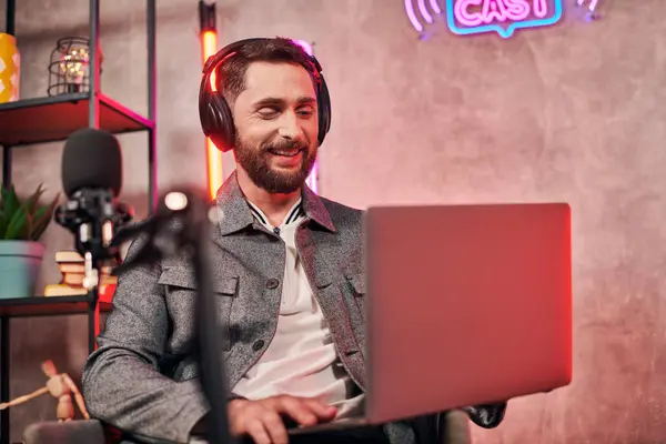 Good looking bearded man in comfy everyday attire sitting with laptop during podcast in studio — Stock Photo