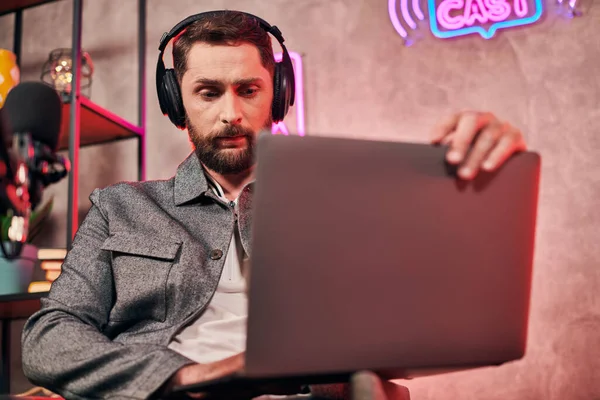 Bell'uomo barbuto in comodo abbigliamento quotidiano seduto con computer portatile durante il podcast in studio — Foto stock
