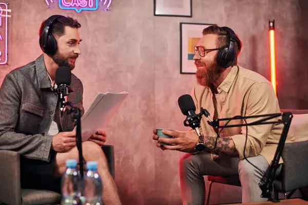 Hombres guapos en atuendos cómodos casuales con auriculares discutiendo preguntas durante el podcast - foto de stock
