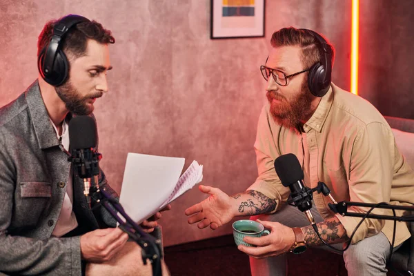 Hombres guapos en atuendos cómodos casuales con auriculares discutiendo preguntas durante el podcast - foto de stock