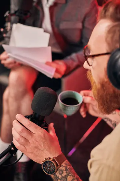 Red haired bearded man with glasses sitting next to his guest during their podcast in studio — Stock Photo