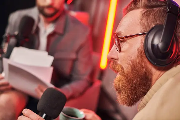 Homme barbu aux cheveux roux avec des lunettes assis à côté de son invité lors de leur podcast en studio — Photo de stock