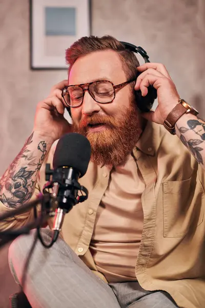 Bel homme aux cheveux roux avec écouteurs en tenue élégante regardant la caméra pendant le podcast — Photo de stock