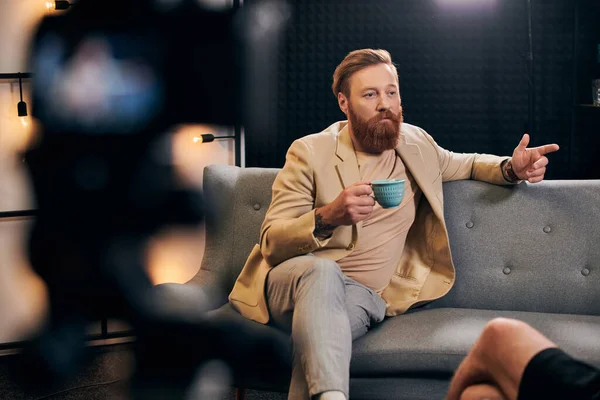 Hombre barbudo guapo con pelo rojo en ropa elegante sentado al lado de su entrevistador en el estudio - foto de stock