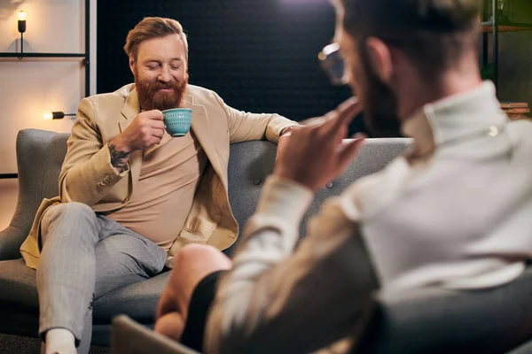 Cheerful bearded man with red hair in elegant clothes sitting next to his interviewer in studio — Stock Photo