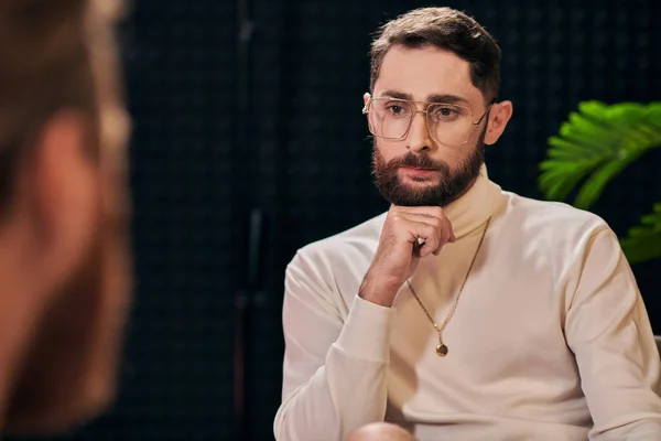 Handsome bearded man with glasses in elegant outfit sitting and looking at his interviewer — Stock Photo