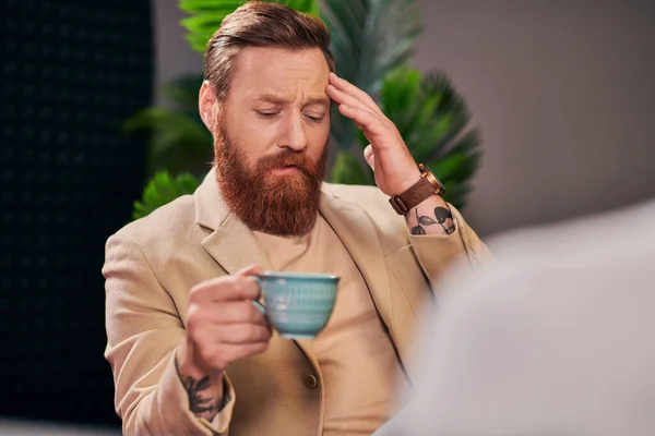 Hombre barbudo bien parecido con taza de café sentado durante la discusión al lado de su entrevistador - foto de stock