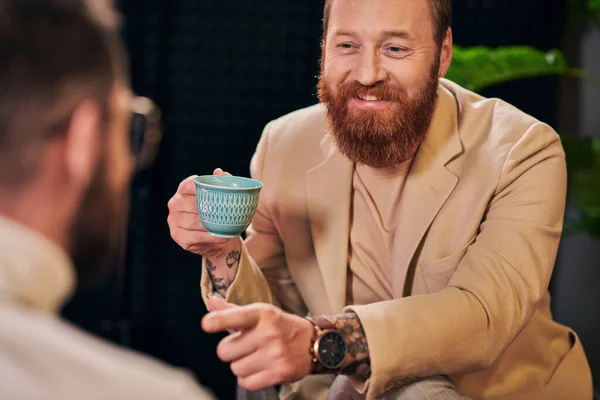 Весёлые мужчины в модной одежде сидят за чашкой кофе и обсуждают вопросы интервью — стоковое фото