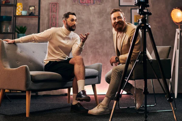 Hombres guapos en ropa de moda con accesorios sentados y discutiendo preguntas de entrevista - foto de stock