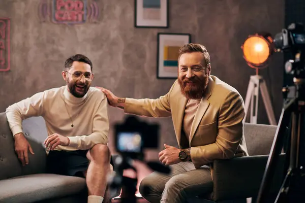 Due uomini barbuti allegri in eleganti abiti eleganti seduti e guardando la fotocamera durante l'intervista — Foto stock