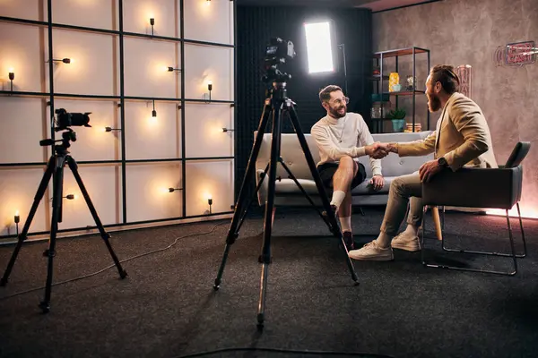 Beaux hommes élégants avec barbe en tenue chic serrant la main lors d'une interview en studio — Photo de stock