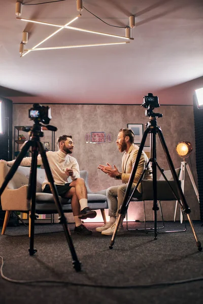 Dos hombres elegantes con barbas con estilo elegante sentado y discutiendo preguntas de la entrevista en el estudio - foto de stock