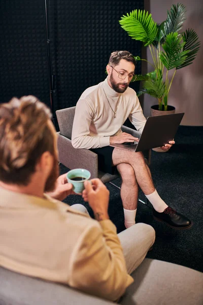 Beaux hommes dévoués en tenues élégantes avec café et ordinateur portable discuter des questions d'entrevue — Photo de stock