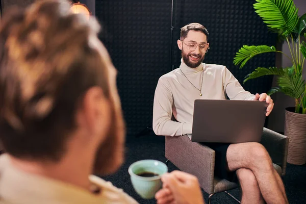 Hombres alegres de buen aspecto en trajes elegantes con café y portátil discutir preguntas de la entrevista - foto de stock