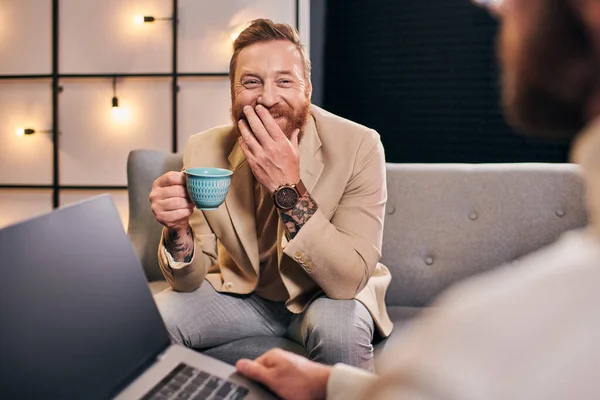 Deux joyeux hommes attrayants dans des vêtements élégants avec café et ordinateur portable discuter des questions d'entrevue — Photo de stock