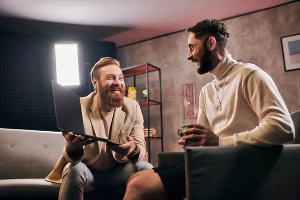 Dos alegres hombres atractivos en trajes elegantes con café y portátil discutir preguntas de la entrevista - foto de stock