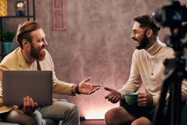 Два веселых красивых мужчины в элегантных одеждах с кофе и ноутбуком обсуждают вопросы интервью — стоковое фото