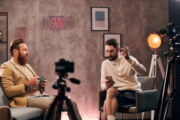 Добре виглядають елегантні чоловіки в шикарних сукнях з бородою, що розмовляють під час інтерв'ю, з кавою та телефоном — стокове фото