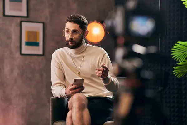 Handsome bearded man with glasses in elegant attire sitting with smartphone in hand during interview — Stock Photo