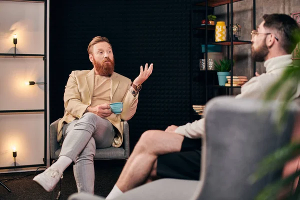 Bel homme roux avec barbe dans des vêtements élégants parler avec son intervieweur tout en studio — Photo de stock
