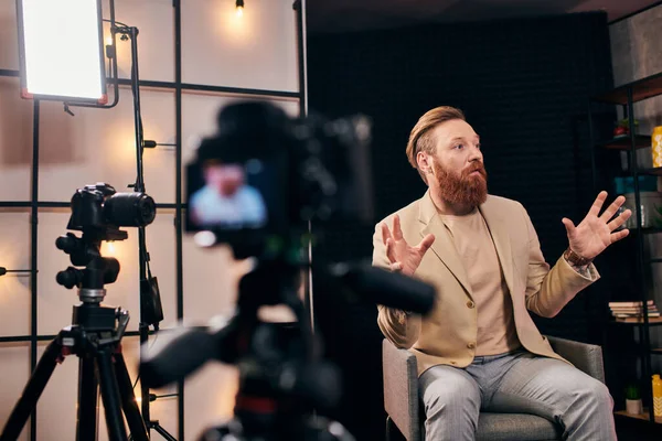 Bell'uomo con i capelli rossi e la barba in abito elegante parlando attivamente durante il podcast in studio — Foto stock