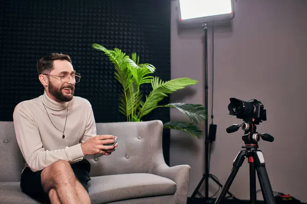 Joyful bearded man in elegant attire with glasses holding coffee cup during interview in studio — Stock Photo