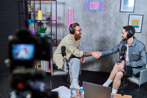 Good looking bearded men in casual comfy attires with headphones shaking hands during podcast — Stock Photo