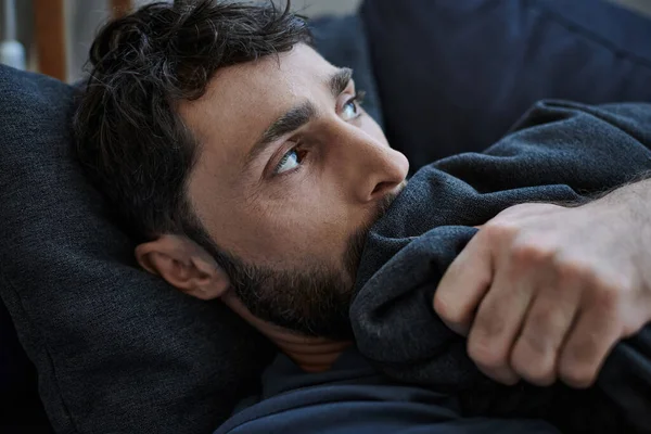 Depressiver bärtiger Mann in lässigem Outfit liegt während des Zusammenbruchs auf Sofa, Bewusstsein für psychische Gesundheit — Stockfoto