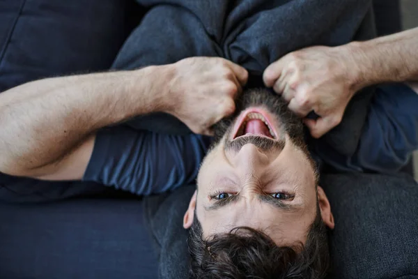 Bearded depressed man in casual clothes screaming while lying on sofa during mental breakdown — Stock Photo