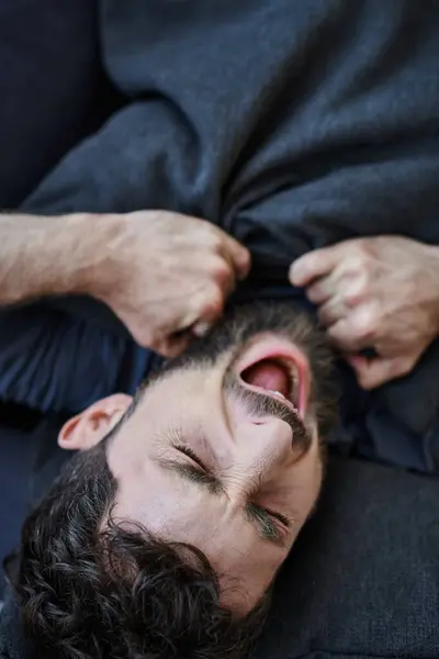 Bärtiger depressiver Mann in Freizeitkleidung schreit, während er während eines Nervenzusammenbruchs auf dem Sofa liegt — Stockfoto