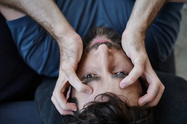 Gestresster verzweifelter Mann mit Bart in Freizeitkleidung, der mit den Händen vor dem Gesicht während eines Nervenzusammenbruchs liegt — Stockfoto