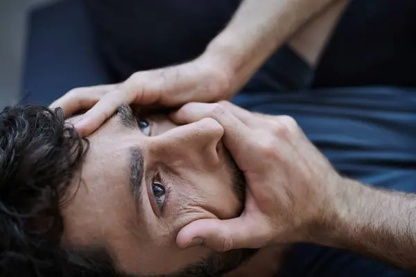 Отчаявшийся мужчина с бородой в повседневной одежде лежит с руками на лице во время психического срыва — стоковое фото