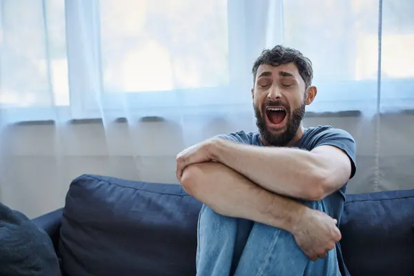 Depressiver traumatisierter Mann in lässigem T-Shirt auf Sofa sitzend und schreiend, Bewusstsein für psychische Gesundheit — Stockfoto