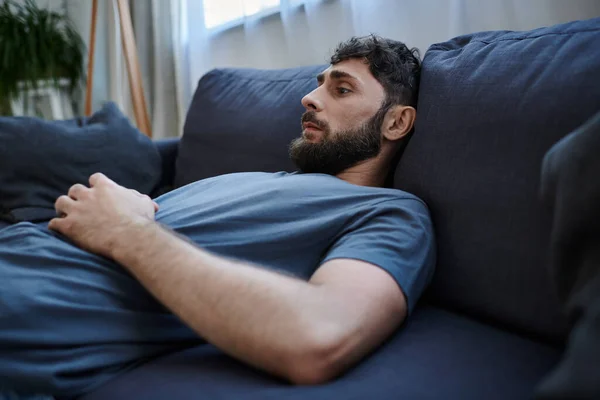 Тревожный отчаявшийся мужчина в домашней одежде лежал на диване во время депрессивного эпизода, психического здоровья осведомленности — стоковое фото