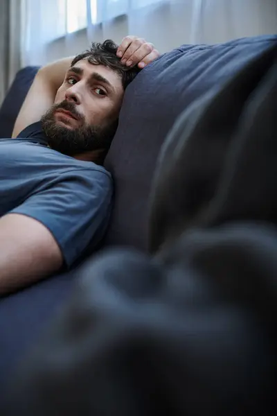 Депресивний безнадійний чоловік у затишному домашньому вбранні лежить на дивані під час психічного розладу, психотерапія — стокове фото