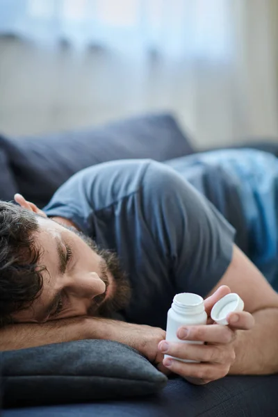 Traumatisierter Mann mit Bart auf Sofa liegend, Tabletten in der Hand, Bewusstsein für psychische Gesundheit — Stockfoto