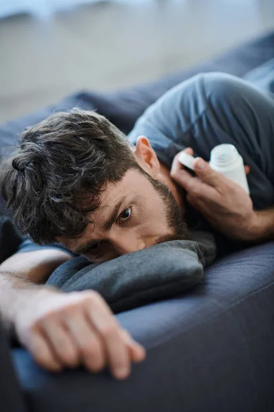 Traumatisierter Mann mit Bart auf Sofa liegend, Tabletten in der Hand, Bewusstsein für psychische Gesundheit — Stockfoto