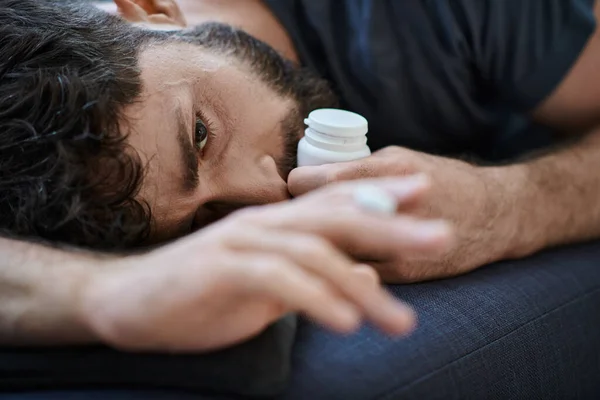 Depressed anxious man in casual attire lying on sofa with pills in hand, mental health awareness — Stock Photo