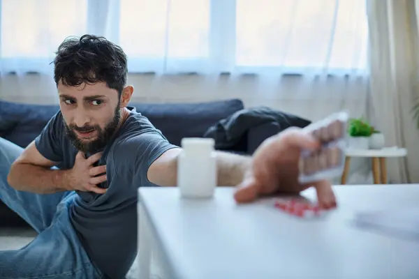 Focus on anxious bearded man with depressive episode reaching to his blurred pills, mental health — Stock Photo