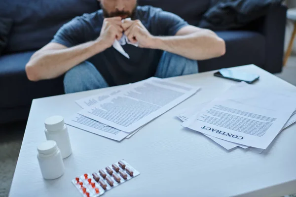 Vista recortada del hombre enfermo sentado en la mesa con papeles y pastillas en él durante la crisis mental - foto de stock