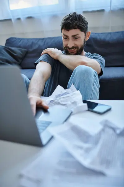 Homem deprimido com sorriso louco em roupa de casa olhando para seu laptop durante colapso, saúde mental — Fotografia de Stock