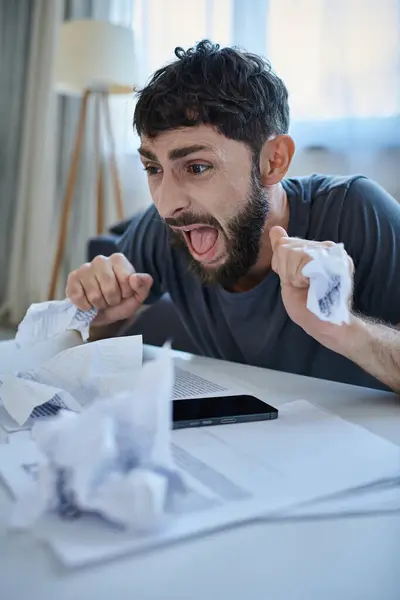 Depressed man sitting at table with papers and phone on it and screaming during mental breakdown — Stock Photo